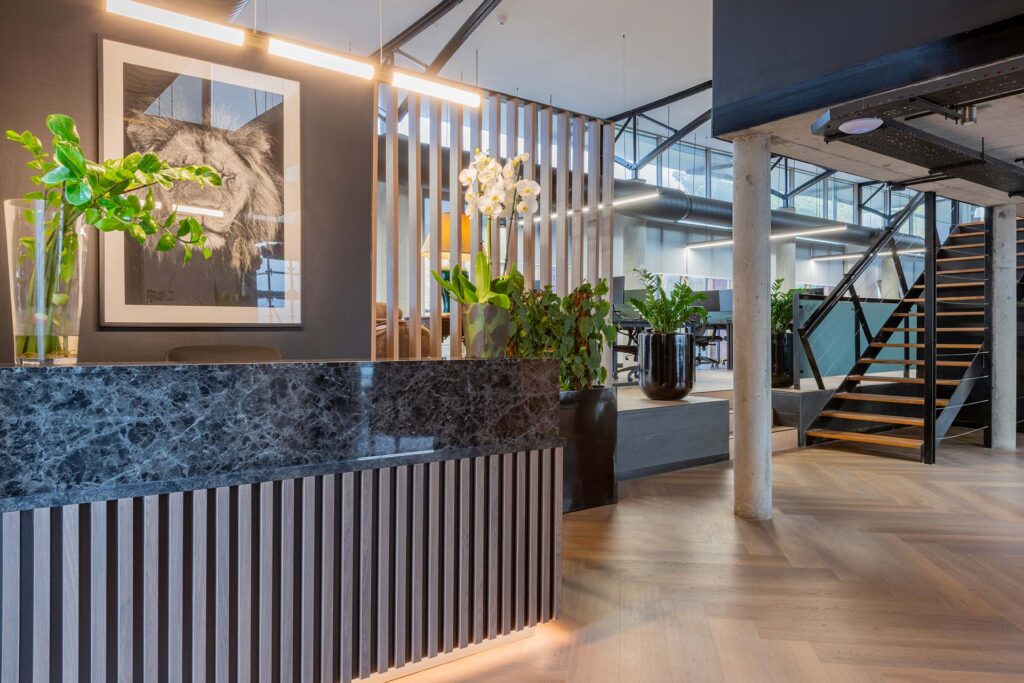 Lionhead Capital luxury office reception desk design with marble stone counter, timber slatted detailing, plants and feature artwork